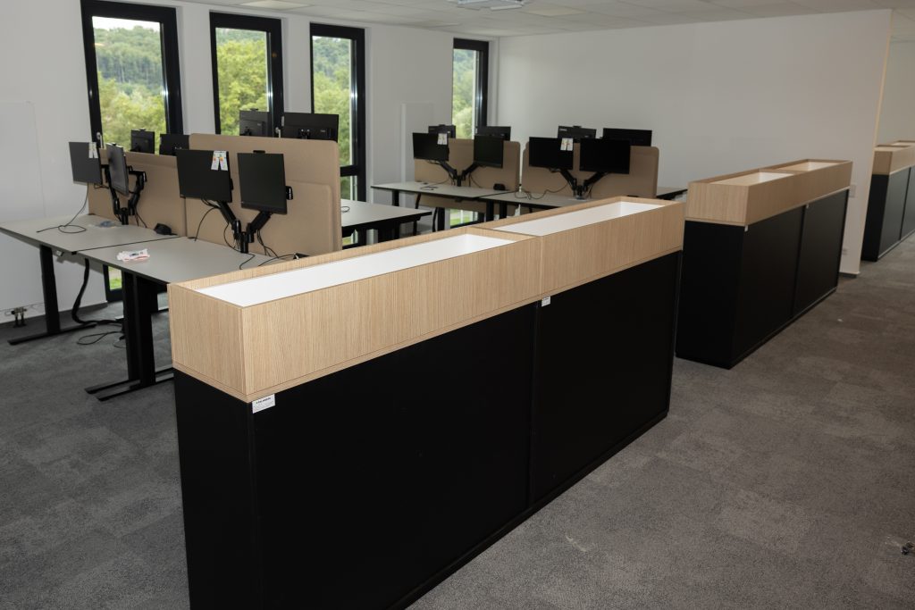 Moderne Büroeinrichtung mit Schreibtischen, Monitoren und ergonomischen Stühlen in heller Arbeitsumgebung