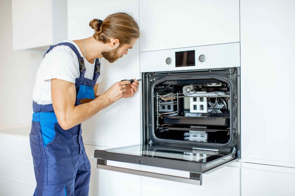 Küchenmonteur installiert Backofen in weißer Einbauküche